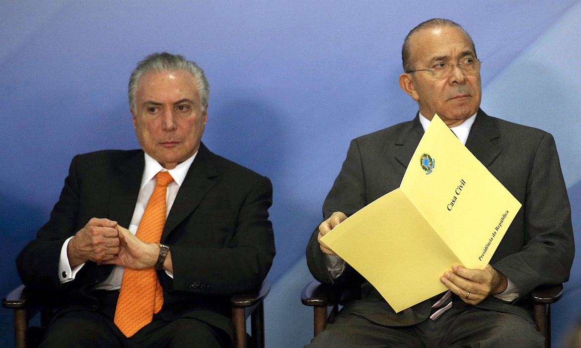 À esquerda, Michel Temer, à direita, Eliseu Padilha, responsável transição de governos em 2018. Foto mostra ambos sentados, com uma parede azul ao fundo.