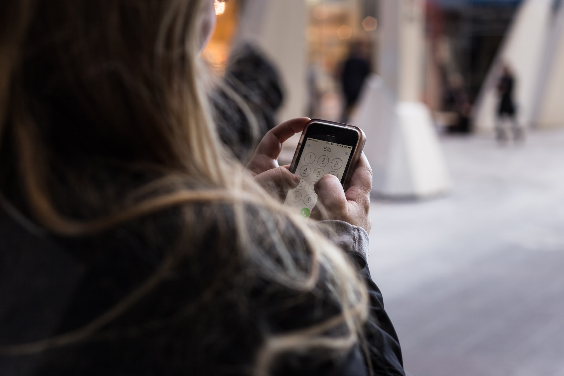mulher de costas mexendo em celular, prestes a efetuar chamada telefônica.