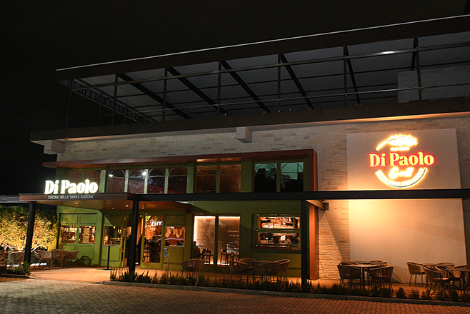 Fachada do Restaurante Galeto Di Paolo, em SJC, com luzes, céu preto, gramado, portas verdes, com detalhes em vidro e teto.