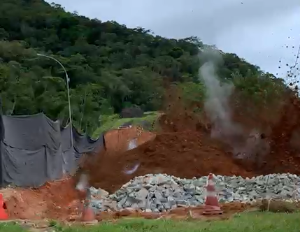 Rocha sendo explodida em Ubatuba, com área verde ao fundo, pedras na frente e barro para o alto.