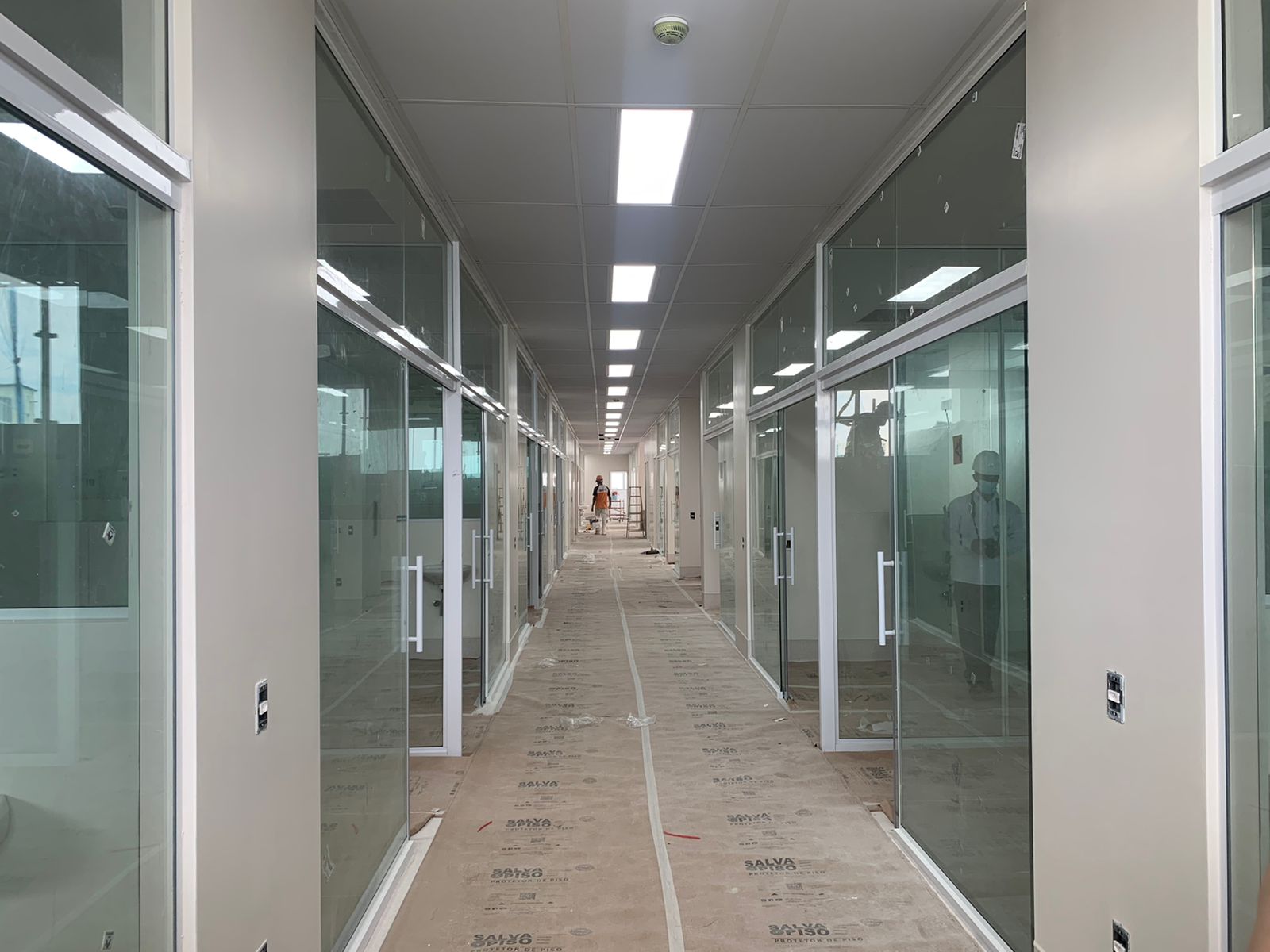 Parte interna da Santa Casa SJC, cuja obra está 95% concluída, com um teto branco, luzes, piso, vidros e funcionários trabalhando.
