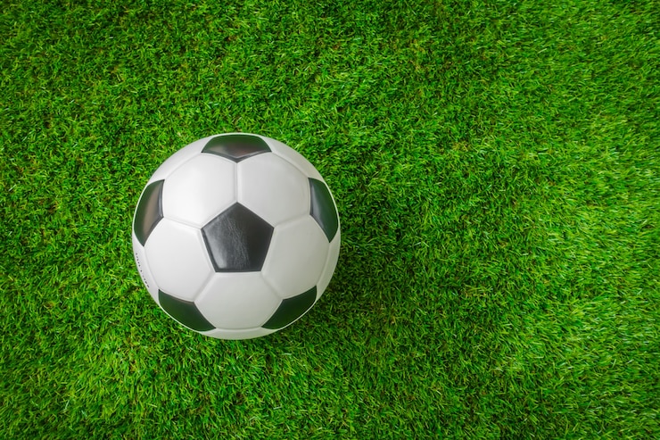 Bola de futebol branca e preta em cima de um gramado verde, sintético.