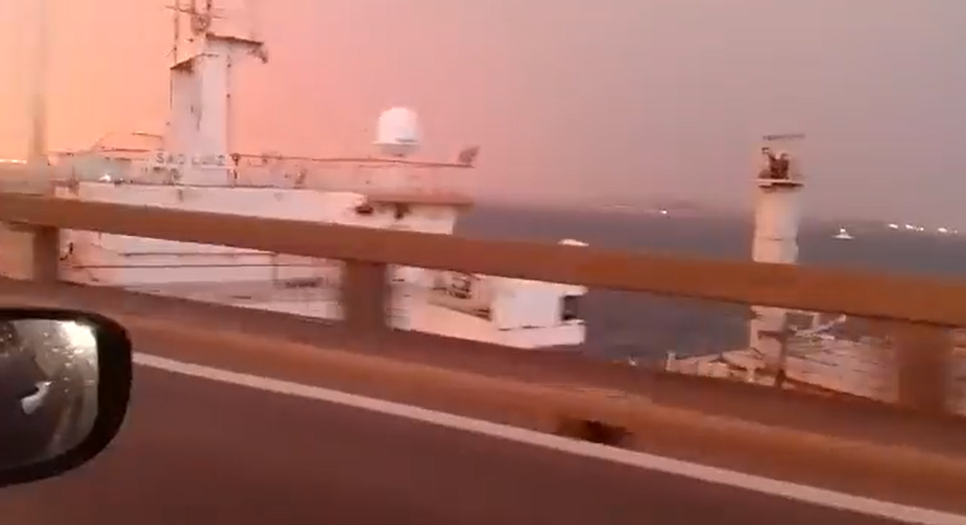 Print do vídeo que mostra um navio colidindo na Ponte Rio-Niterói, sobre o mar, gravado de um veículo, com o retorvisor no canto.