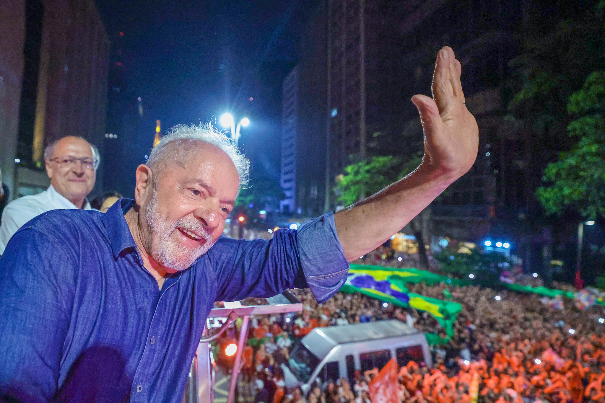 Presidente eleito, Luiz Inácio Lula da Silva (PT) discursando na Avenida Paulista após vitória nas eleições de 2022. Ele stá ao lado do vice, Gerlado Alckmin (PSB) em carro espécie de trio elétrico e fala para uma multidão de pessoas.