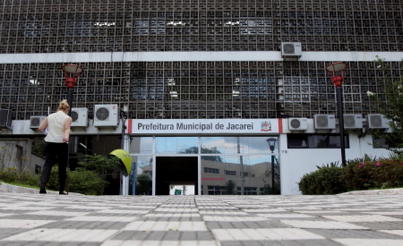 Fachada da Prefeitura de Jacareí, com cores cinzas e uma mulher andando; foto ilustra a matéria que diz que o salário do prefeito terá aumento.