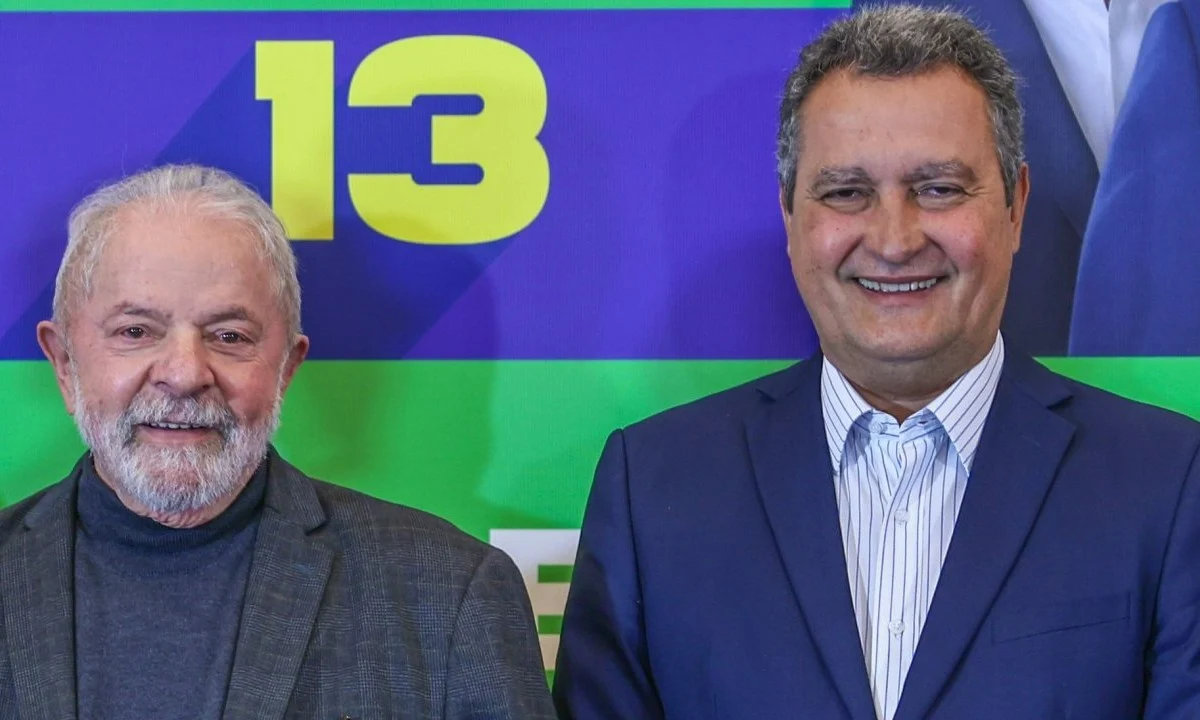 Lula ao lado de Rui Costa, em um fundo azul, amarelo e verde; foto ilustra a matéria que diz que o Governo Lula terá 37 ministérios.