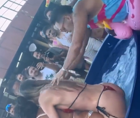 Foto mostra momento em que Tirullipa é expulso da Farofa da Gkay por puxar biquíni de influencers, com piscina, água e pessoas em volta.