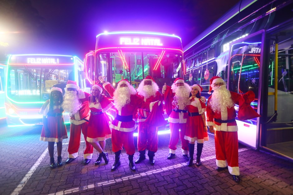 Caravanas de Natal em SJC, com Papais Noel na frente de ônibus iluminados.