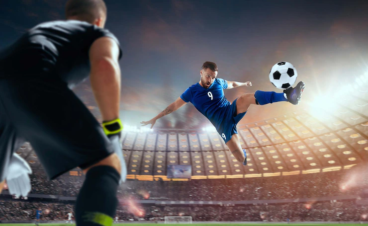 Homem de uniforme azul chutando uma bola preta e branca, em um estádio.