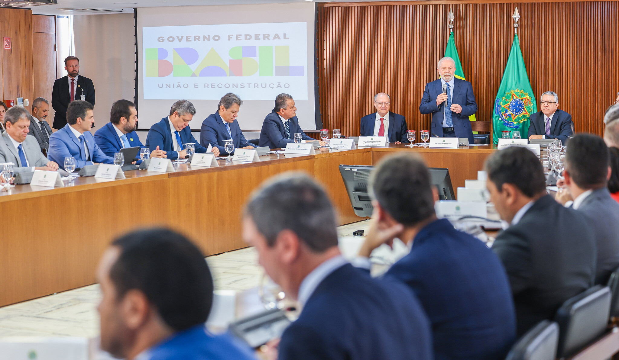 Reunião entre Lula e governadores dos estados do Brasil, com parede marrom ao fundo e pessoas sentadas na bancada.