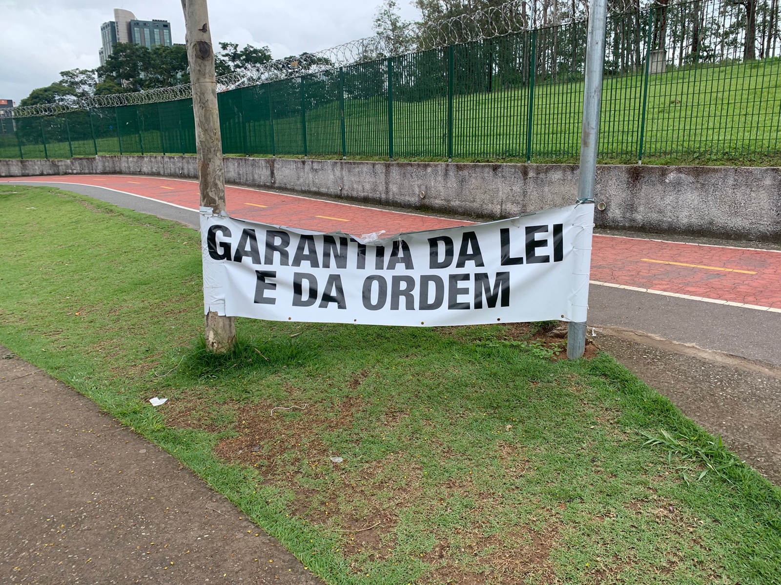 Outra foto de uma das placas em frente ao DCTA, em SJC, pedindo "garantia da Lei e da Ordem", em cima de um gramado e uma pista de corrida no fundo.