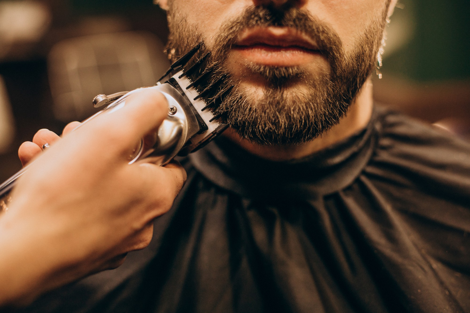 Homem com barba, vestimenta preta, no barbeiro, com uma máquina de barbear; foto ilustra a matéria sobre as Oficinas Reinvente, de Pindamonhangaba.