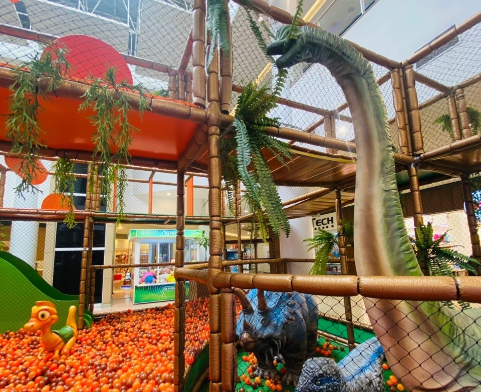 Buriti Shopping Guará terá dinossauros neste mês de férias; foto mostra piscina de bolinhas laranja, dinossauro verde e rede.