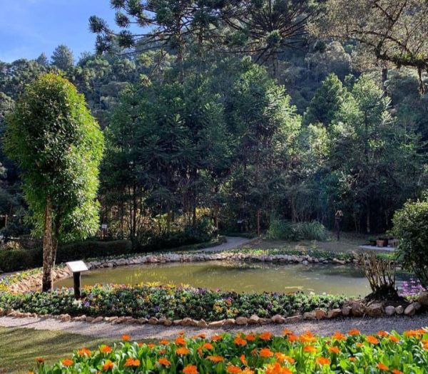 imagem de um bosque, com lago e árvores em volta, flores bem coloridas; foto ilustra a matéria de parques para curtir em Campos do Jordão.