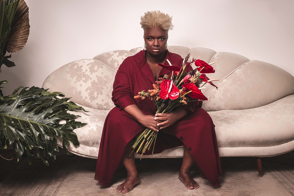 cantora ellen oléria de vermelho sentada sobre sofá branco e segurando um grande buquê de rosas
