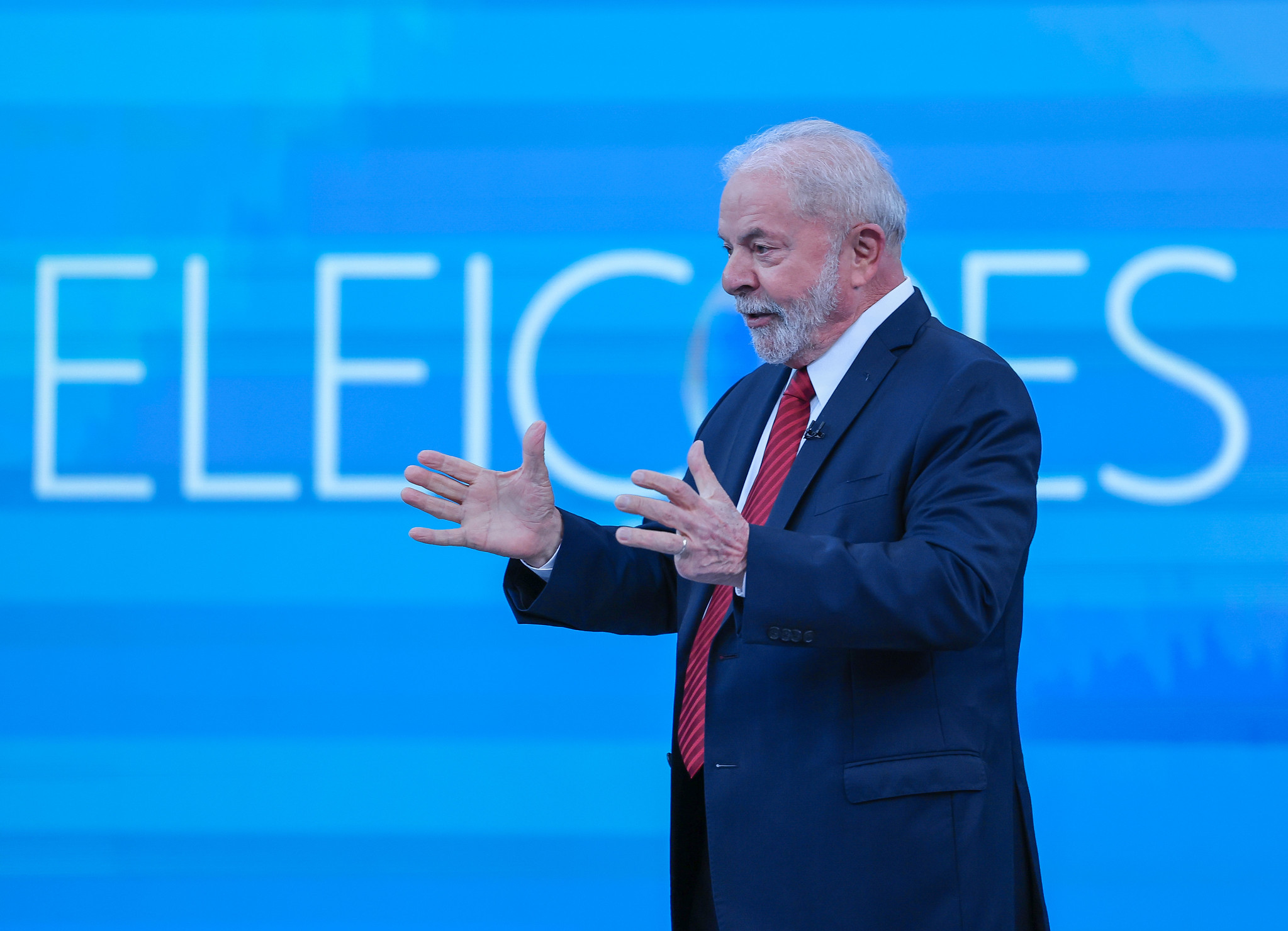 Lula com terno preto, camisa branca, gravata vermelha e olhando para a esquerda, em frente a uma tela azul; foto ilustra matéria sobre o Acordo de Genebra, referente ao aborto.