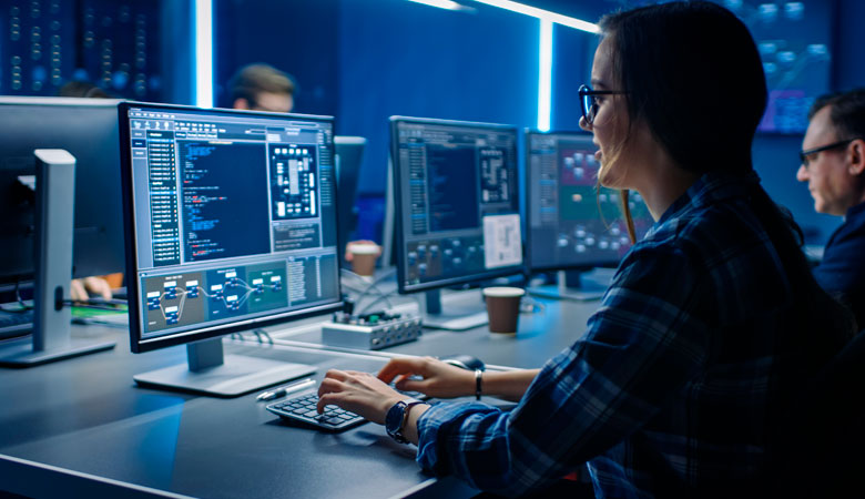 Mulher trabalhando em um computador, com cenário azul, dados na tela e outras pessoas em volta. Foto ilustra matéria sobre os cursos para trabalhar na SSP23, na Space Studies Program, em São José dos Campos.