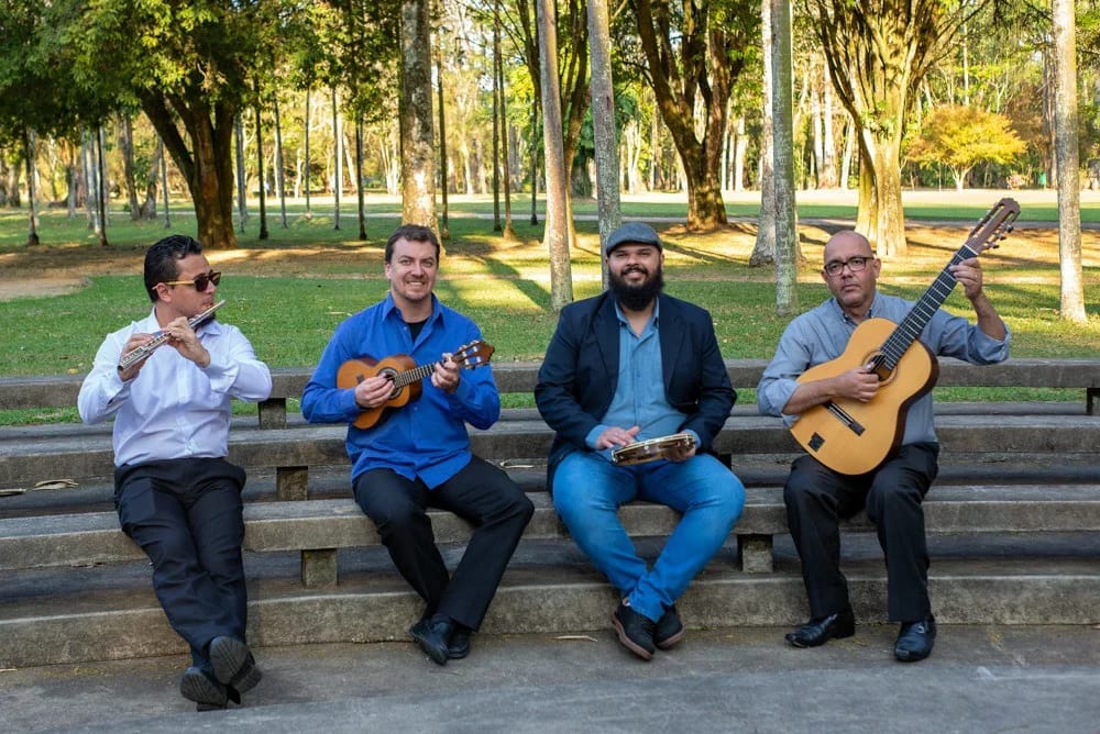 Grupo Conversa Afiada, que realizará a próxima roda de choro no bar Disk Me Disse, em São José dos Campos; foto mostra os integrantes sentados em um tronco, com seus instrumentos nas mãos.