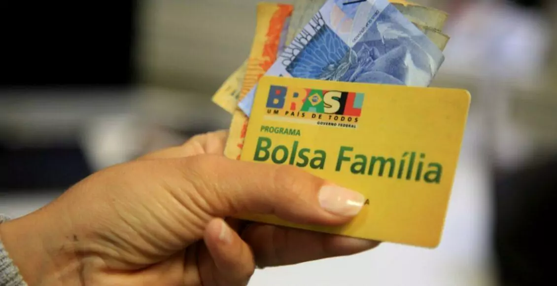 imagem de uma mão com cédulas de dinheiro e o cartão do programa Bolsa Família