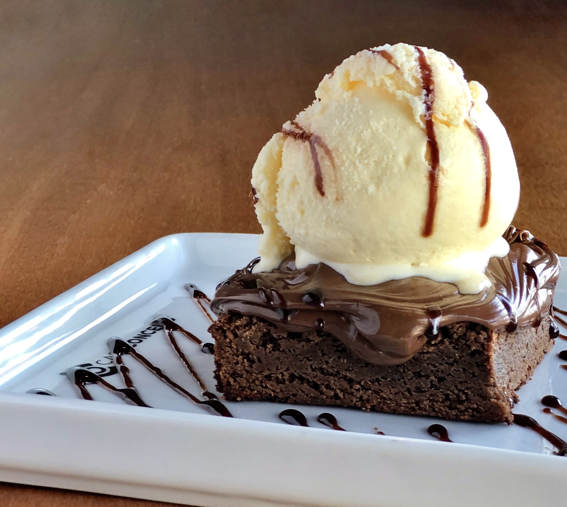 Bolo de chocolate com cobertura e uma bola de sorvete em cima, com uma mesa de madeira ao fundo, no Café Conceito no Taubaté Shopping.
