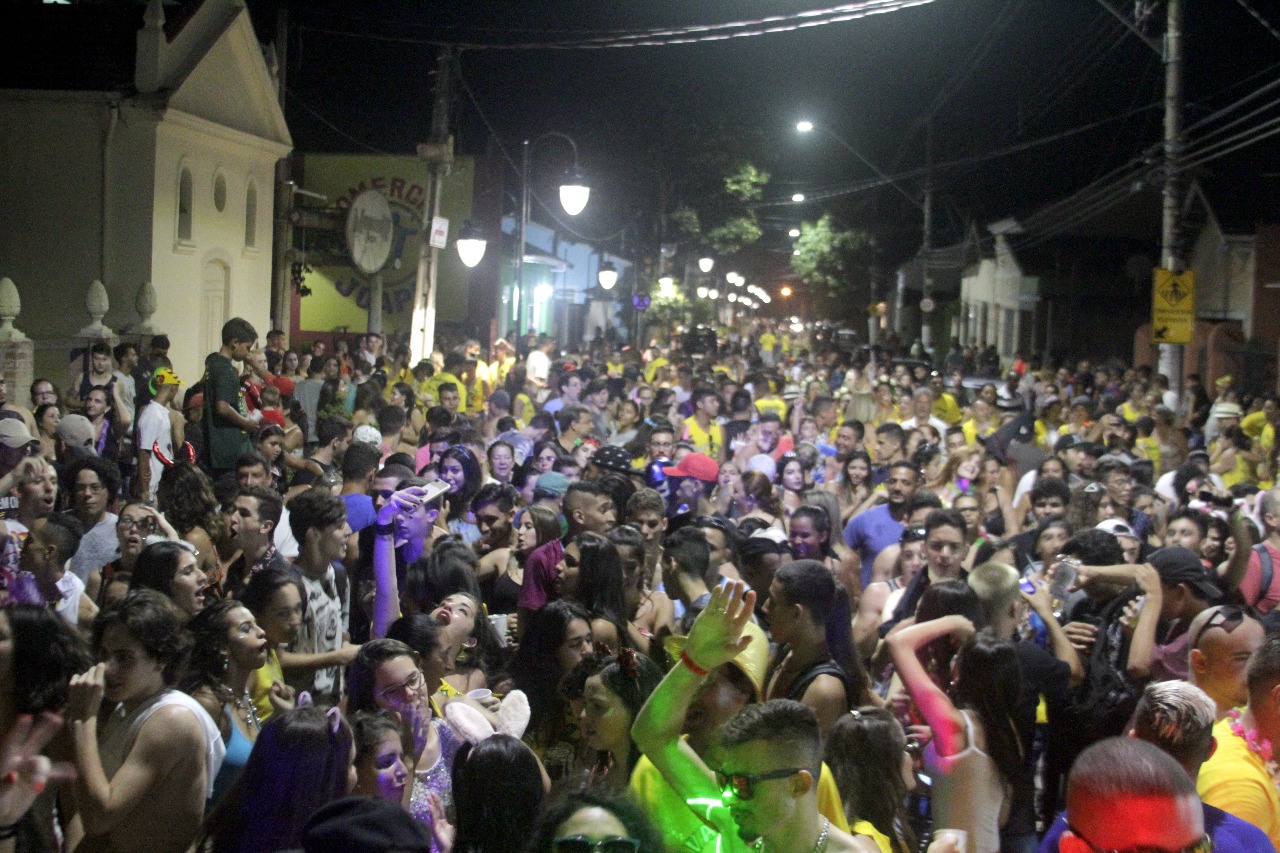 Carnaval em Quiririm no ano de 2018, com diversas pessoas na rua, de noite, com céu preto e luzes ao fundo.