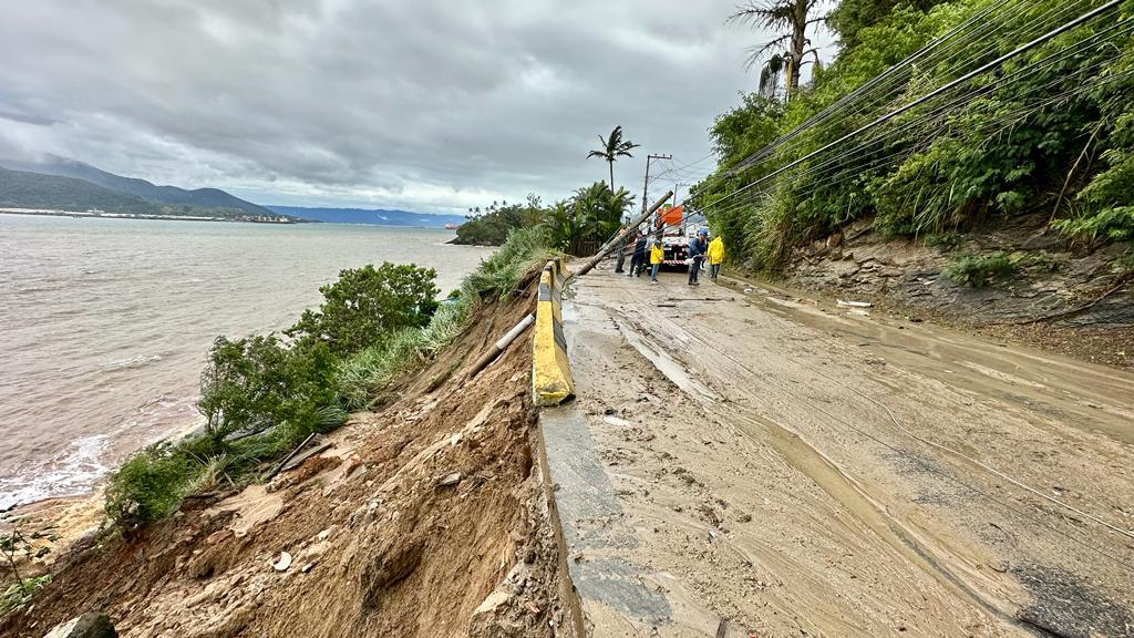 Rua suja de lama devido à chuva em Ilhabela, que também atingiu outras cidades do Litoral Norte paulista. Foto mostra área verde na lateral direita e carros ao fundo.