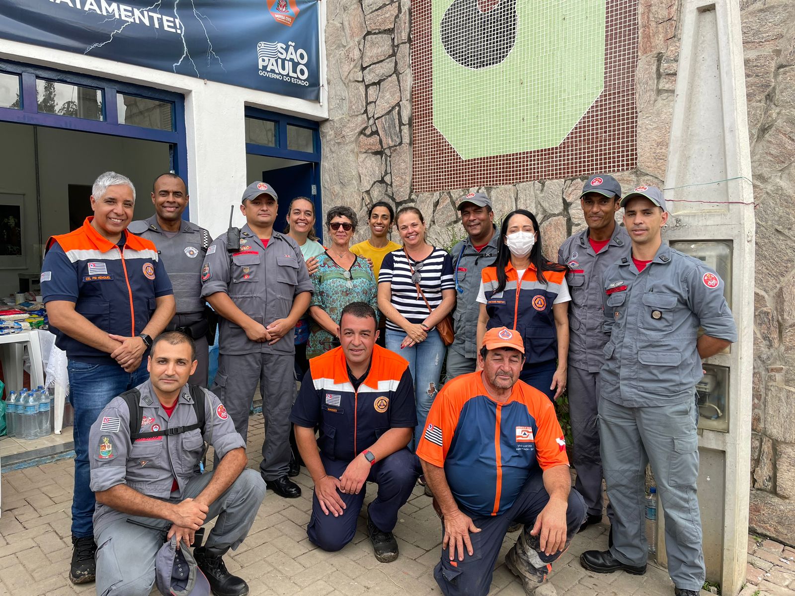 Autoridades do estado de São Paulo e bombeiros visitam áreas afetadas pela chuva em São Luiz do Paraitinga; foto mostra pessoas reunidas em frente a uma parede de pedra, inclusive bombeiros e moradores.