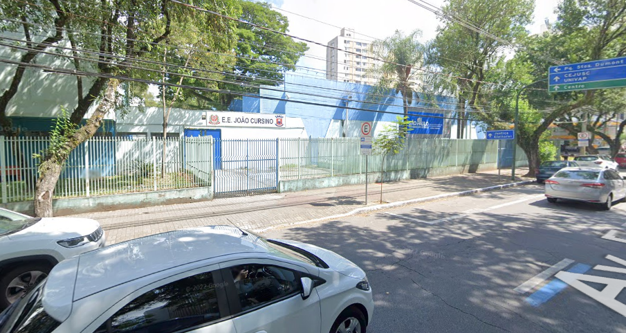 Fachada da Escola Estadual João Cursino, em SJC; rede retoma suas aulas nesta sexta-feira, 3 de fevereiro; foto mostra carros passando na rua, parede azul, céu azul e árvores.