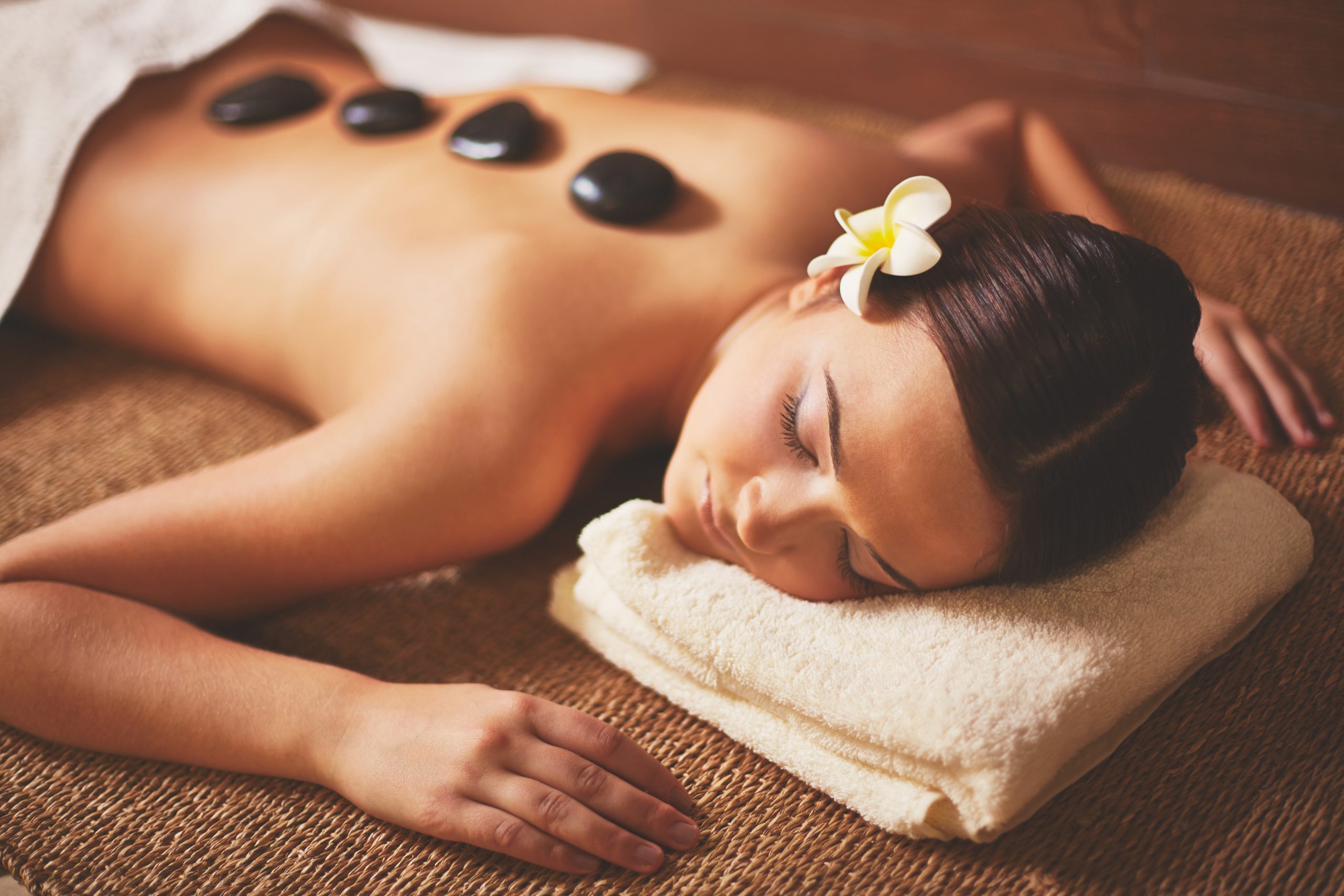 Mulher deitada em uma área de say spa, com uma flor no cabelo e sabonetes nas costas.