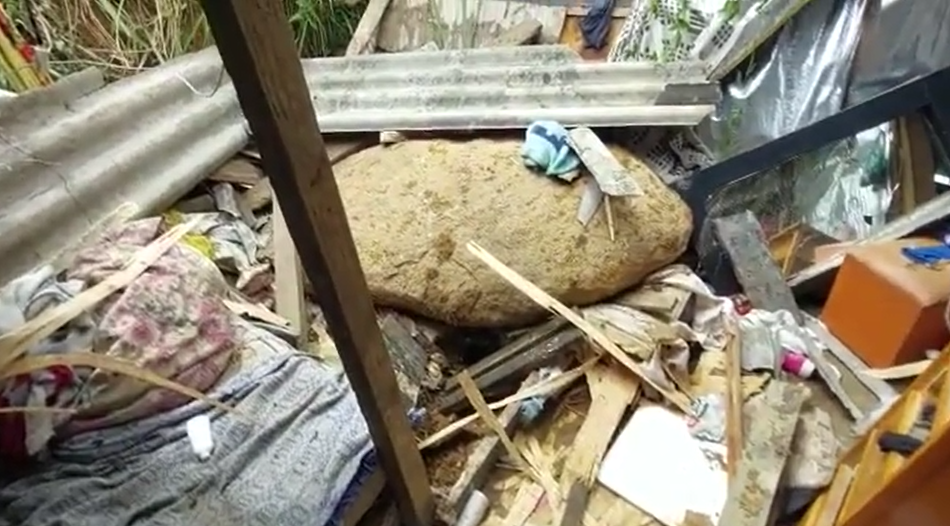 Pedra que deslizou e matou menina de 7 anos em Ubatuba, devido às fortes chuvas no Litoral Norte de São Paulo. Foto mostra a pedra no meio de roupas e galhos de árvore.