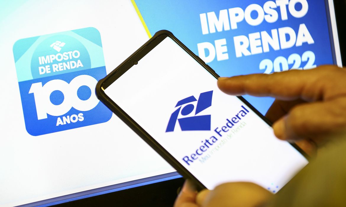 foto de uma mão mexendo no celular com template da Receita Federal; foto ilustra matéria sobre consulta ao lote residual de restituição do Imposto de Renda Pessoa Física (IRPF).