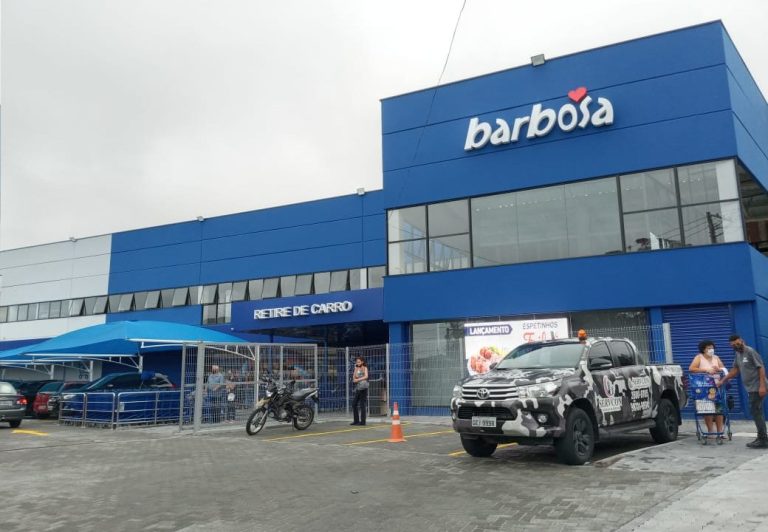 Fachada do Barbosa Supermercados, em São José dos Campos, com céu azul, carros estacionados na frente e asfalto; foto ilustra matéria sobre emprego em SJC (São José dos Campos).