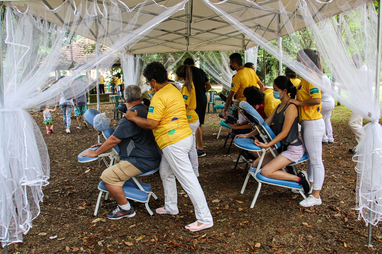 Ação da Unimed São José dos Campos será realizada no Parque Vicentina Aranha; foto mostra pessoas com camiseta amarela, calça branca, chão de terra e teto cinza.