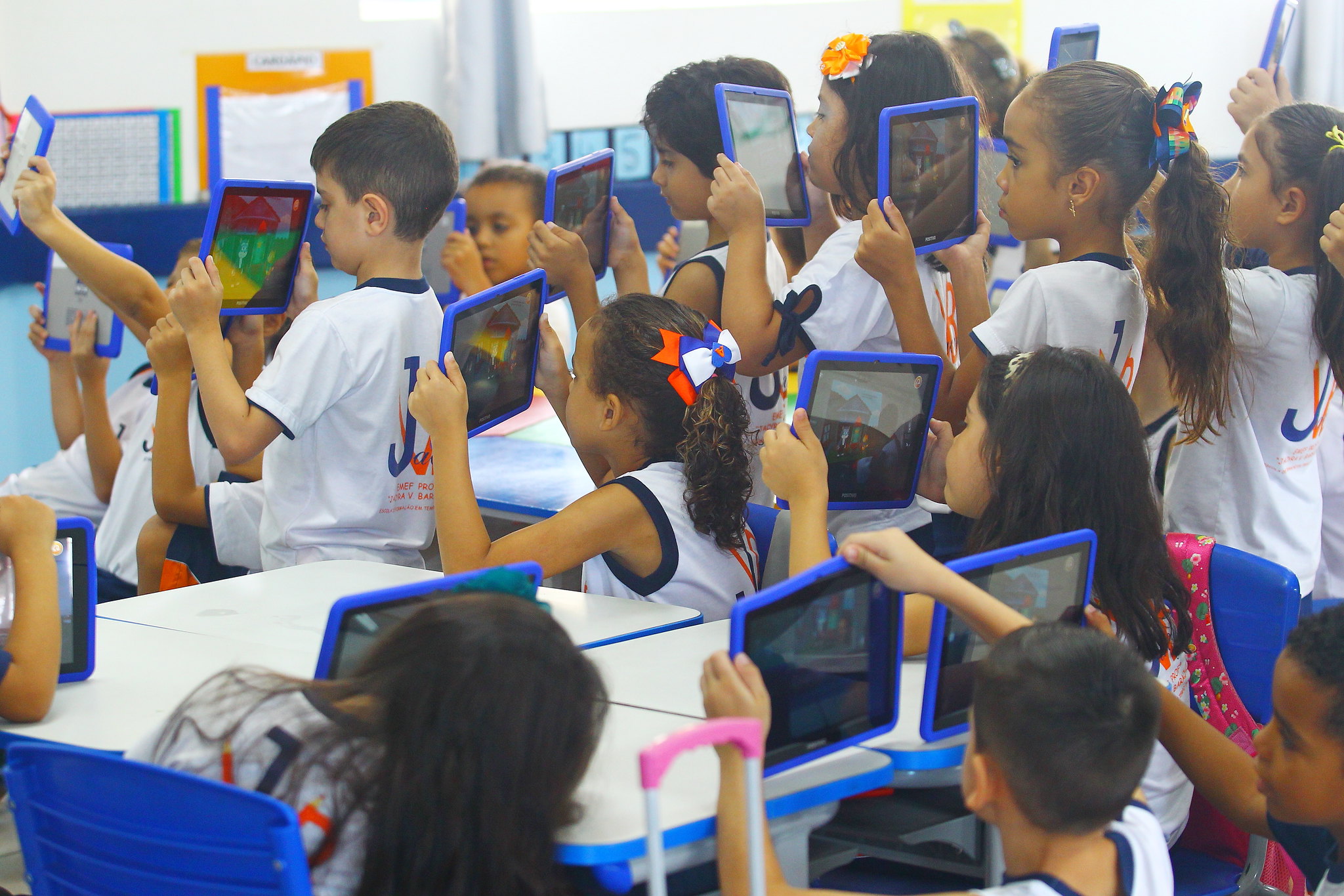 alunos do ensino fundamental em sala de aula segurando tablet virados para a lousa.