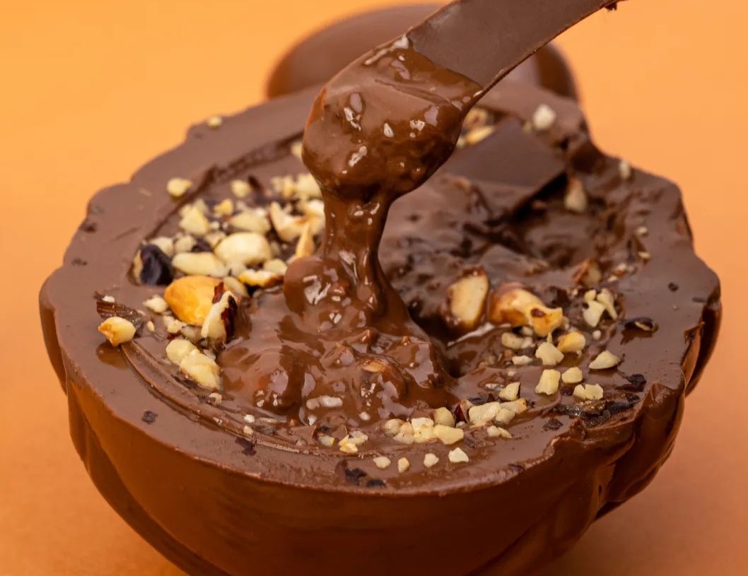 Produto da Chocolate Lugano, com calda e nozes, em um fundo laranja, ilustrando matéria sobre descontos na semana da mulher.