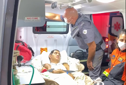 Foto ilustra matéria com o título "Famílias desabrigadas são levadas para hotéis em São Sebastião", com um homem deitado em uma maca de ambulância e um policial ao lado.