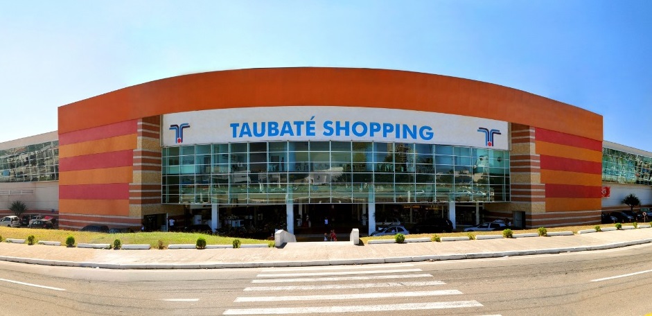 Fachada do Taubaté Shopping, com céu azul, pista na frente, faixa de pedestres e jardim; foto ilustra matéria sobre concurso de biografias do livro Elas, de Patrícia Lopes.