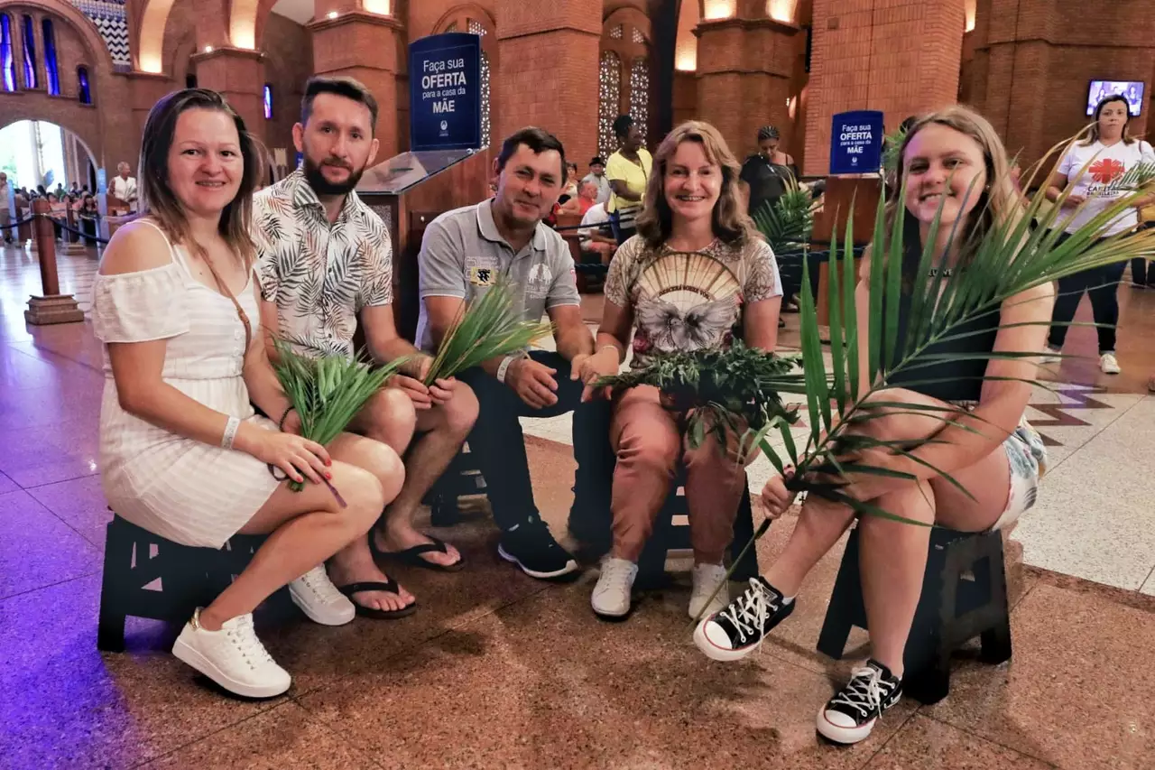 Família Liebel, de Mafra (SC), durante visita à Basílica de Aparecida, antes da celebração do Domingo de Ramos, que abre a Semana Santa; foto mostra paredes marrons e pessoas sentadas com um ramo na mão.