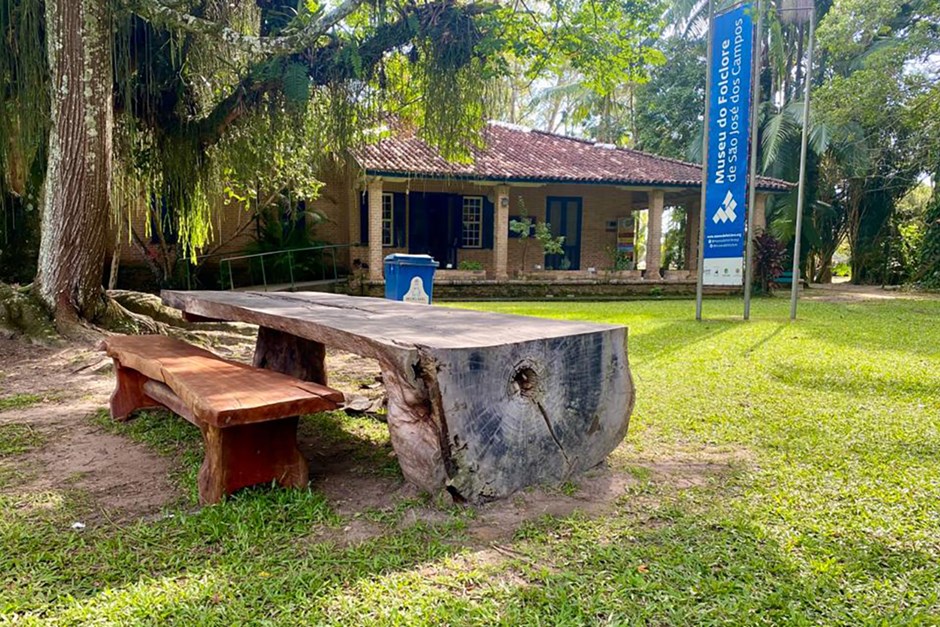 Novos bancos e mesas instalados no Parque da Cidade de São José dos Campos, em madeira, posicionados um ao lado do outro, próximo ao Museu do Folclore, em cima de um gramado verde e árvores ao redor.