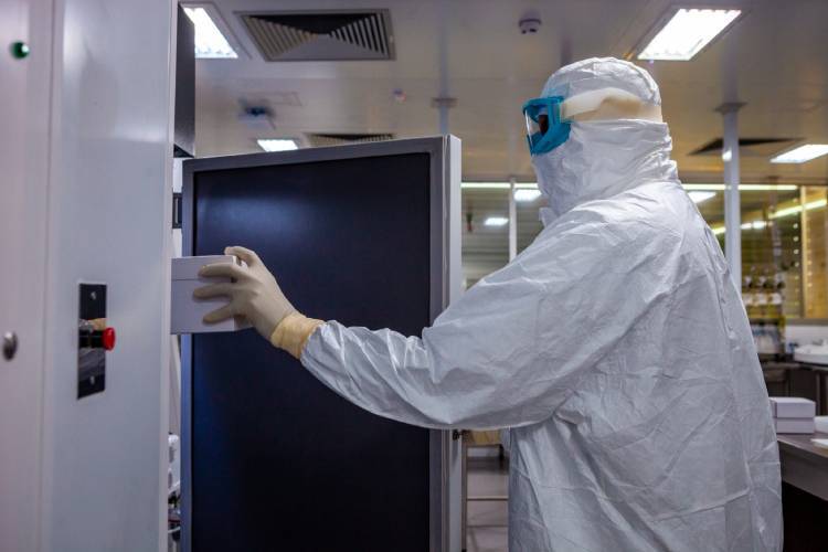 pesquisador paramentado com máscara e roupa de proteção em laboratório.