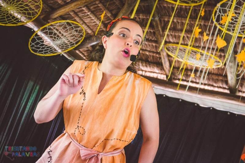 Mulher com uma roupa laranja, em pé, falando no microfone, contando uma história; foto ilustra ação do CenterVale Shopping, em São José dos Campos.
