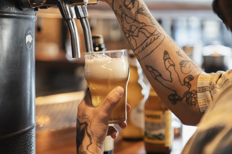 homem tatuado enchendo copo de cerveja em máquina. apenas seus braços são visíveis e ele aparece visto de lado.