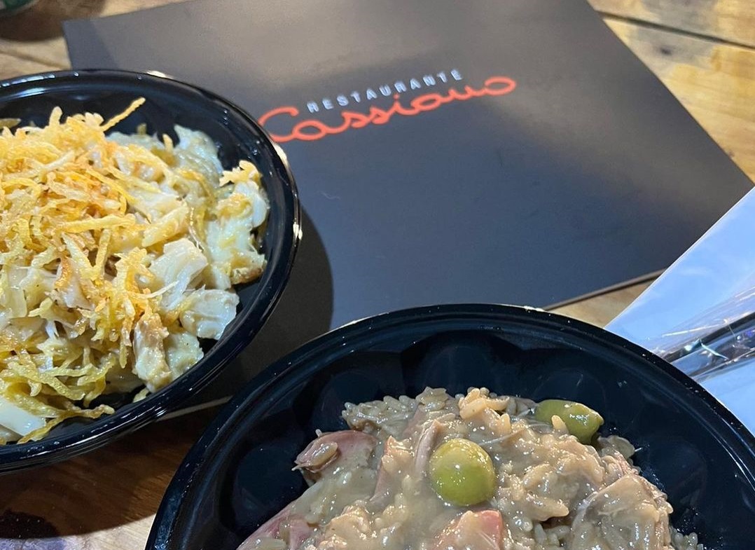 Comidas do Restaurante Cassiano, de São José dos Campos (SJC), durante festival +Gastronomia, anteriormente chamado de Destination, no Parque Vicentina Aranha; foto mostra pratos nas cores pretas com um cardápio ao fundo.