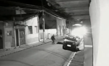 Frame do vídeo que mostra homem agredindo mulher em uma rua em Caçapava, em preto e branco, com casas ao redor.