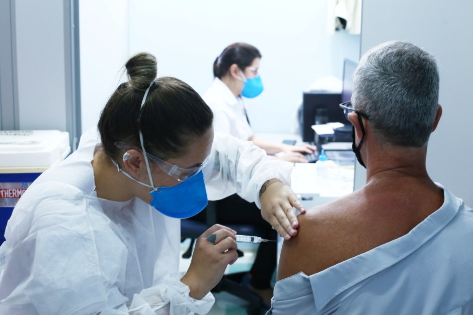 profissional da saúde aplicando imunizante contra a covid-19 em adulto.