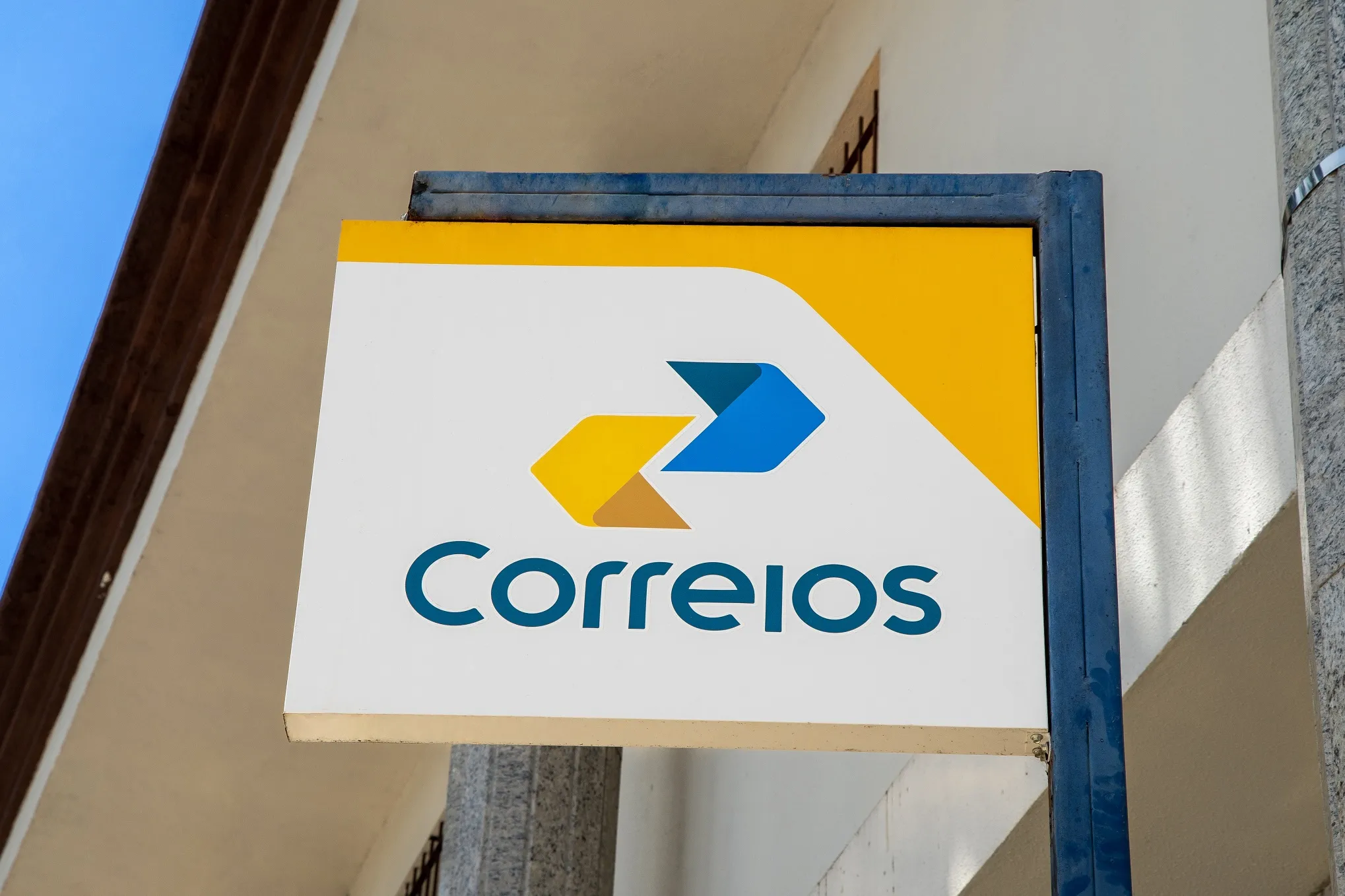 Placa do Correios em branco, amarelo e azul, com um céu azul ao fundo; foto ilustra matéria sobre empregos de Jovem Aprendiz no Vale do Paraíba (São José dos Campos e região).
