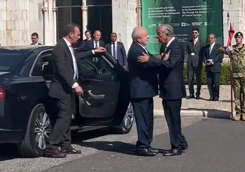 Chegada de Lula em Portugal; foto mostra carro preto e homens de terno em volta.