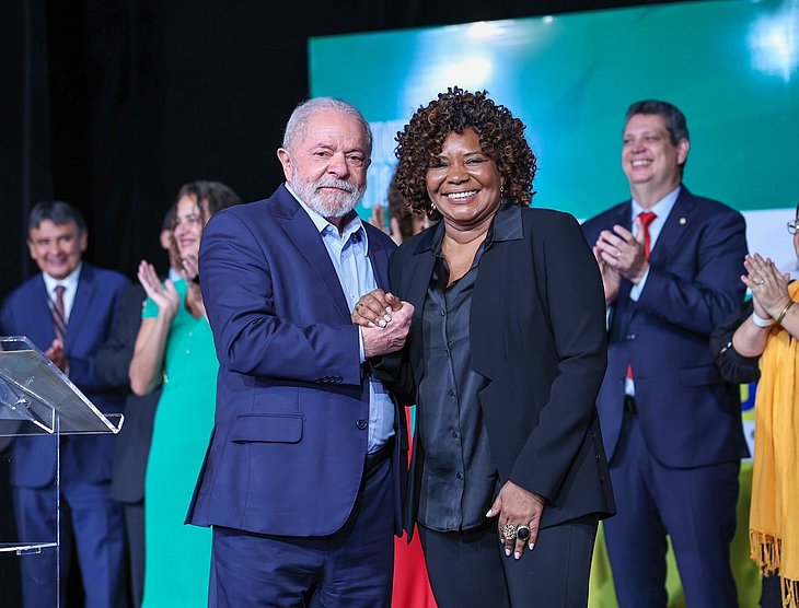 Margareth Menezes ao lado de Lula em um evento, com pessoas ao fundo os aplaudindo; foto ilustra matéria sobre aumento do valor do cachê na Lei Rouanet, anunciado pelo Governo Federal.