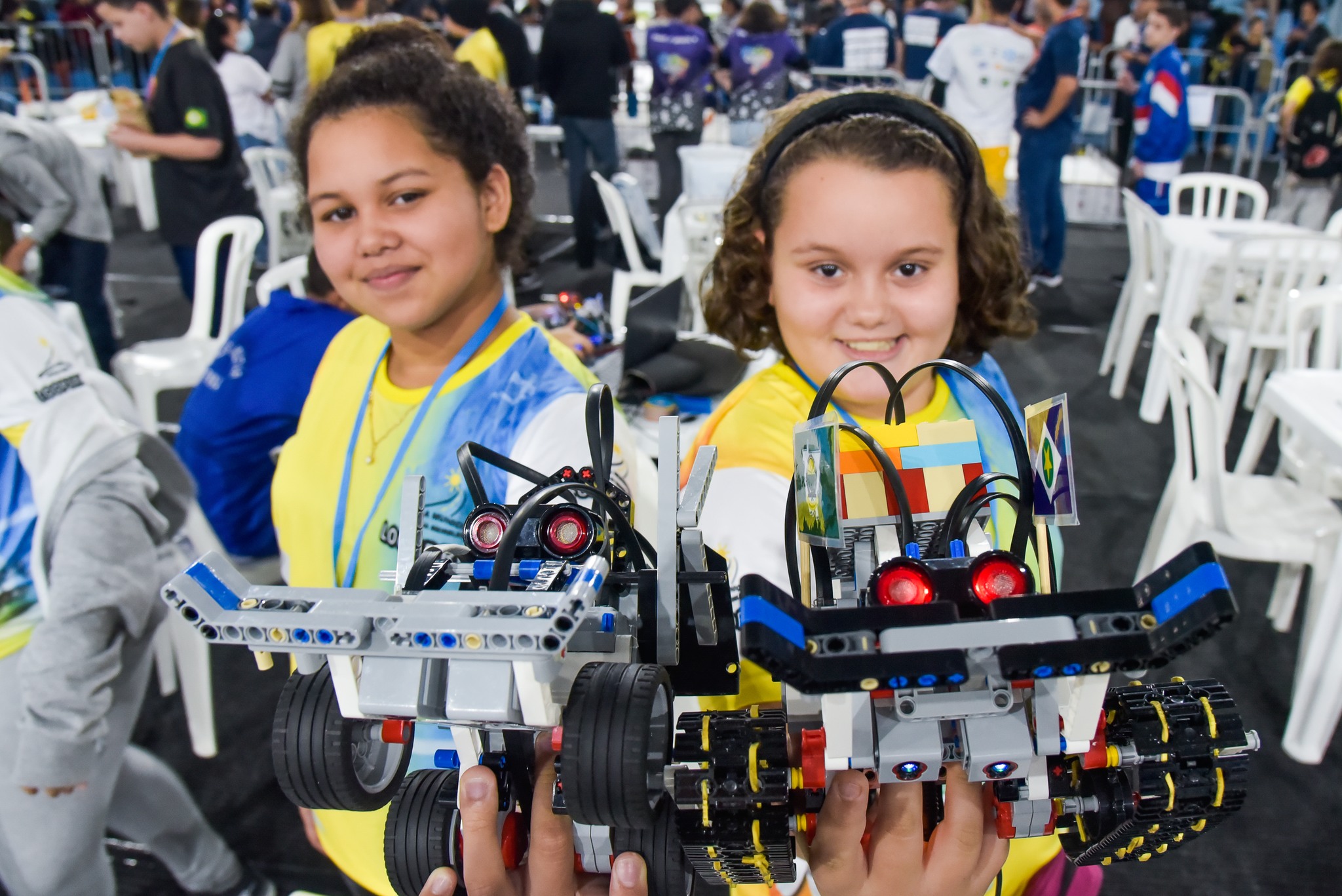 Meninas participantes da Olímpiada Brasileira de Robótica; foto ilustra abertura das inscrições da edição 2023 e mostra alunas segurando um equipamento, olhando para a câmera e com roupas amarelas.
