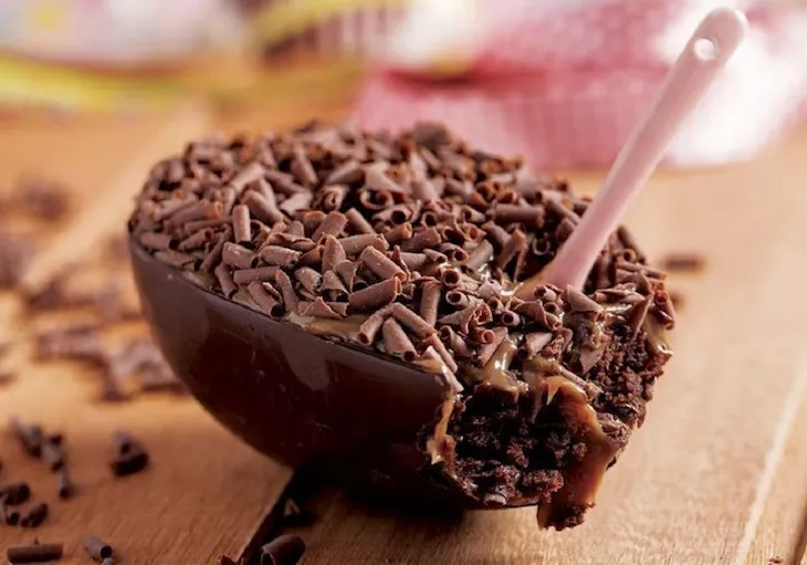 Foto mostra um ovo de Páscoa trufado, com pedaços de chocolate e uma colher branca nele, em cima de uma mesa de madeira, ilustrando matéria sobre vendas no CenterVale Shopping, em São José dos Campos.